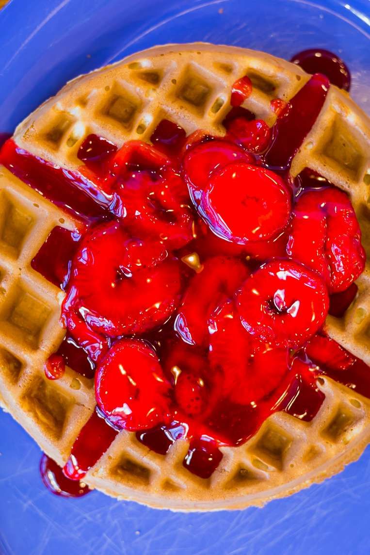 Belgian waffle topped with strawberries on a blue plate